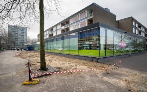 Een foto van de situatie voor de werkzaamheden. We zien een gebouw, een boom en een stuk bestrating.