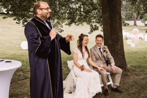 Trouwambtenaar Basti Baroncini spreekt terwijl een bruidspaar naast hem zit